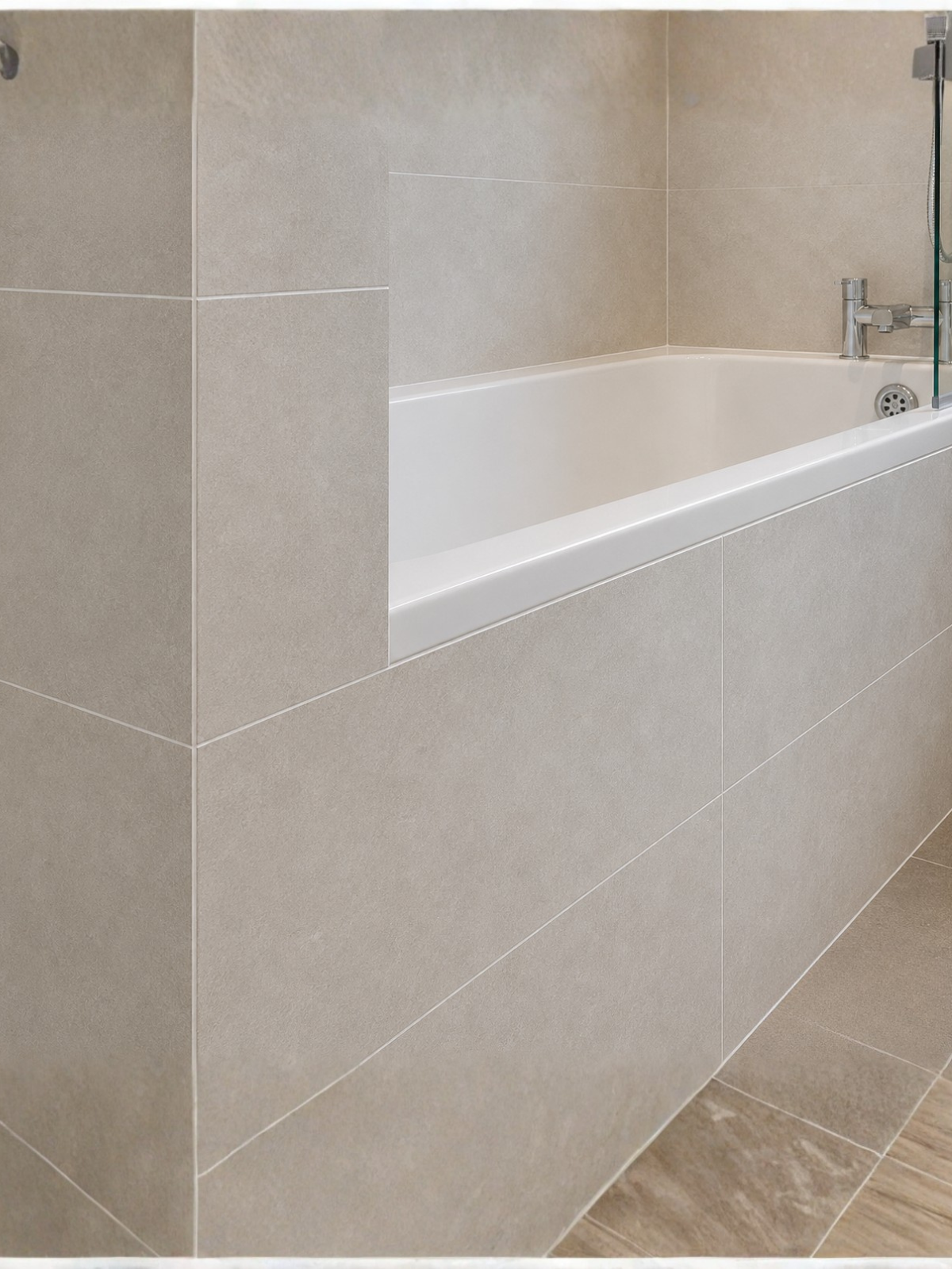 Close-up of professional bathroom tiling in Aylesbury by SN Plumbing Solutions — large-format beige tiles fitted around a modern bath.
